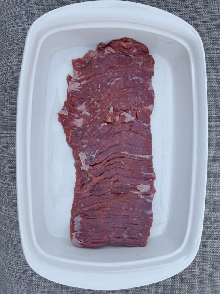 Raw skirt steak in a white baking pan for how to cook skirt steak article.