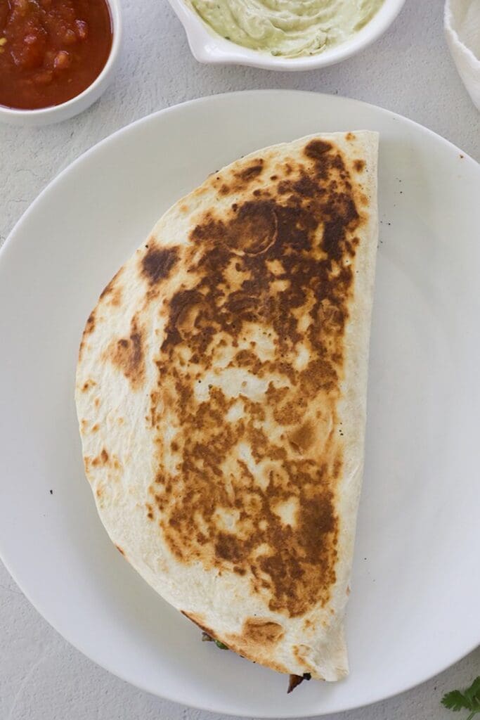 Cooked quesadilla with shredded beef on a white plate.