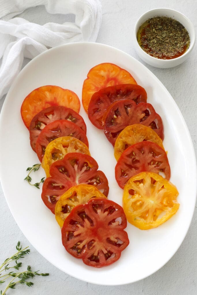 Plate of sliced heirloom tomatoes with a cup of dressing.
