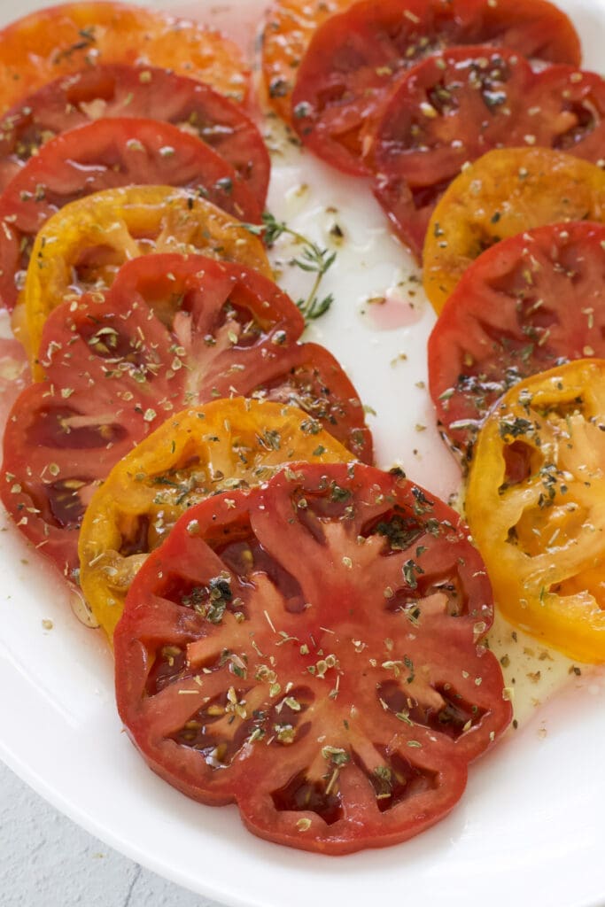 Sliced marinated tomatoes on a white platter.