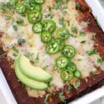 Tray of shredded beef enchiladas topped with jalapenos and avocado slices.