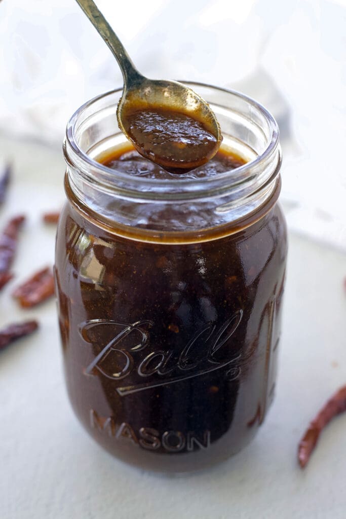 Spoon scooping out red sauce out of a clear jar.