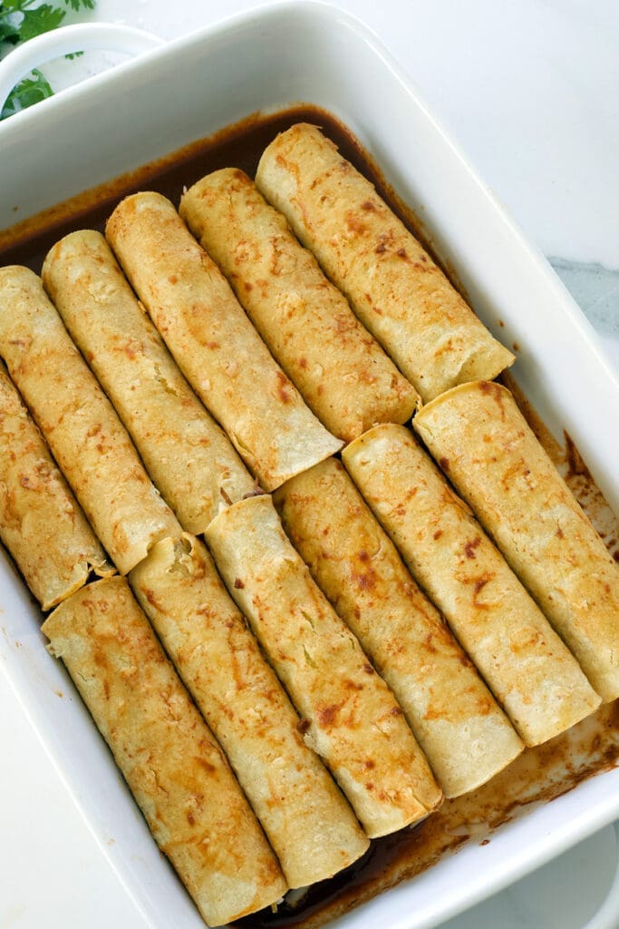 Rolled enchiladas in a white baking dish.
