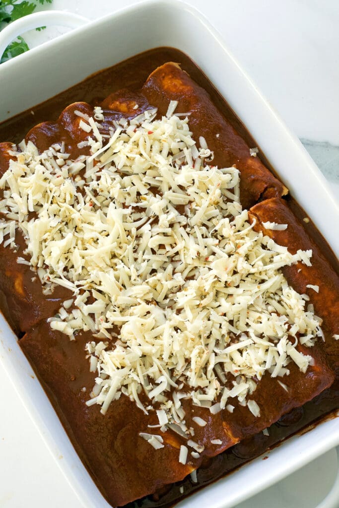 Unbaked beef enchiladas topped with shredded cheese.