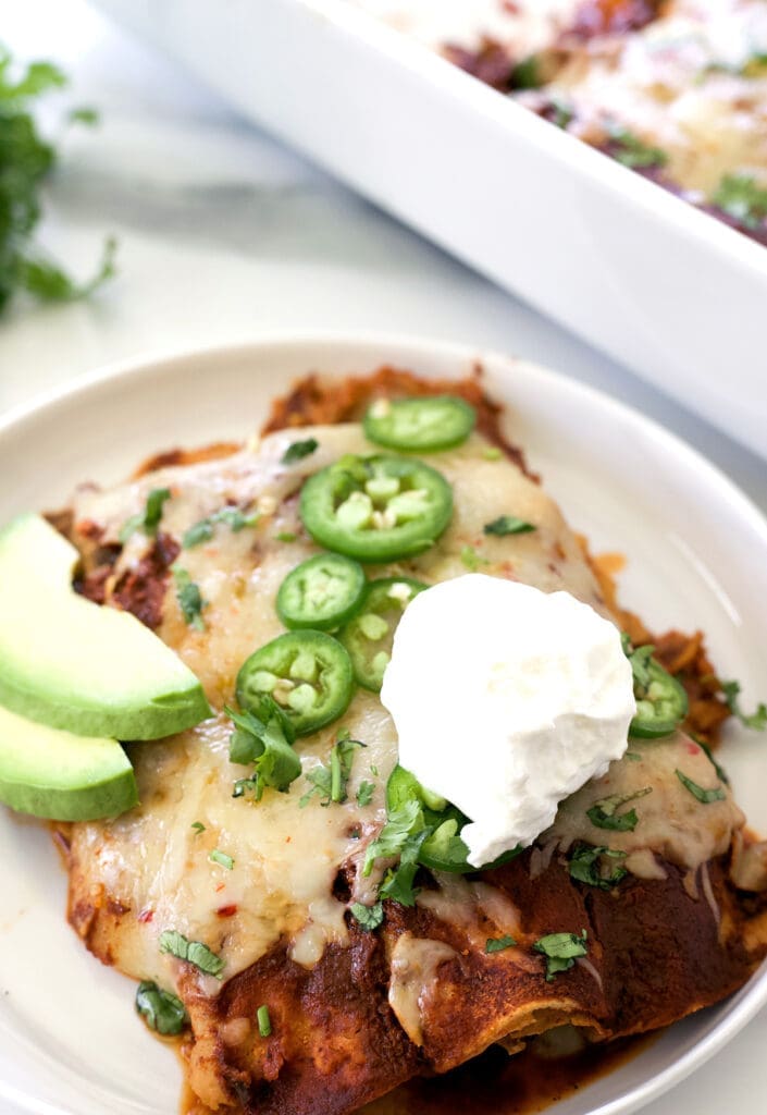 Plate of shredded beef enchiladas topped with sour cream, jalapenos and avocado.